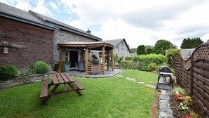 A backyard with a wooden picnic table, a stone wall, and a covered patio area. - Beautiful Holiday Home in Belgium (Bertrix)