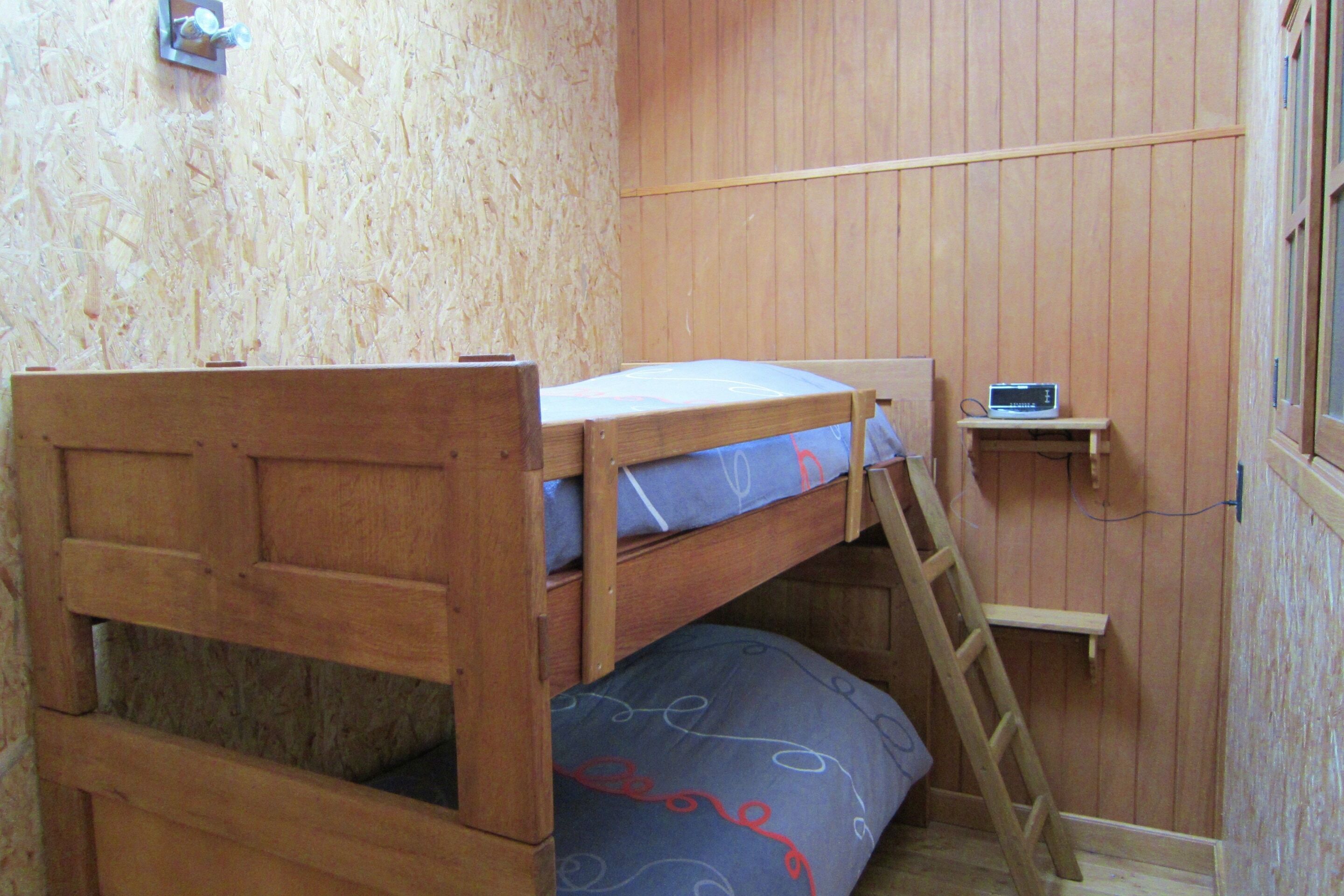 A bunk bed with a ladder, a small shelf with a radio, and a wooden wall.