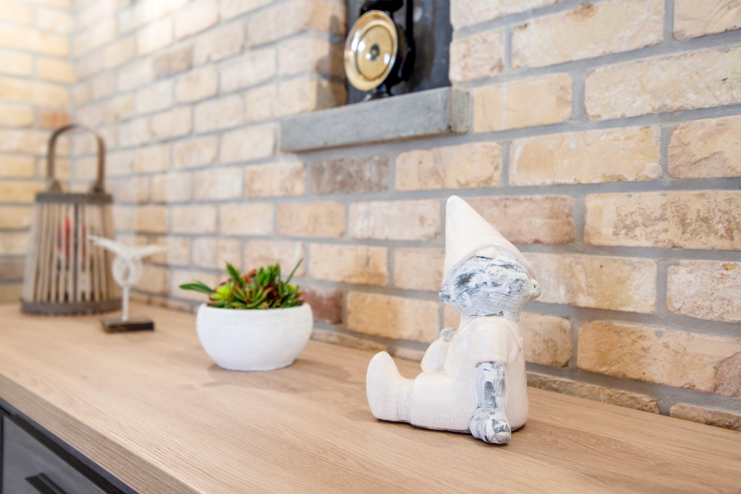 Un comptoir de cuisine avec un mur en briques, une sculpture en céramique blanche, une plante en pot et un objet décoratif en métal.