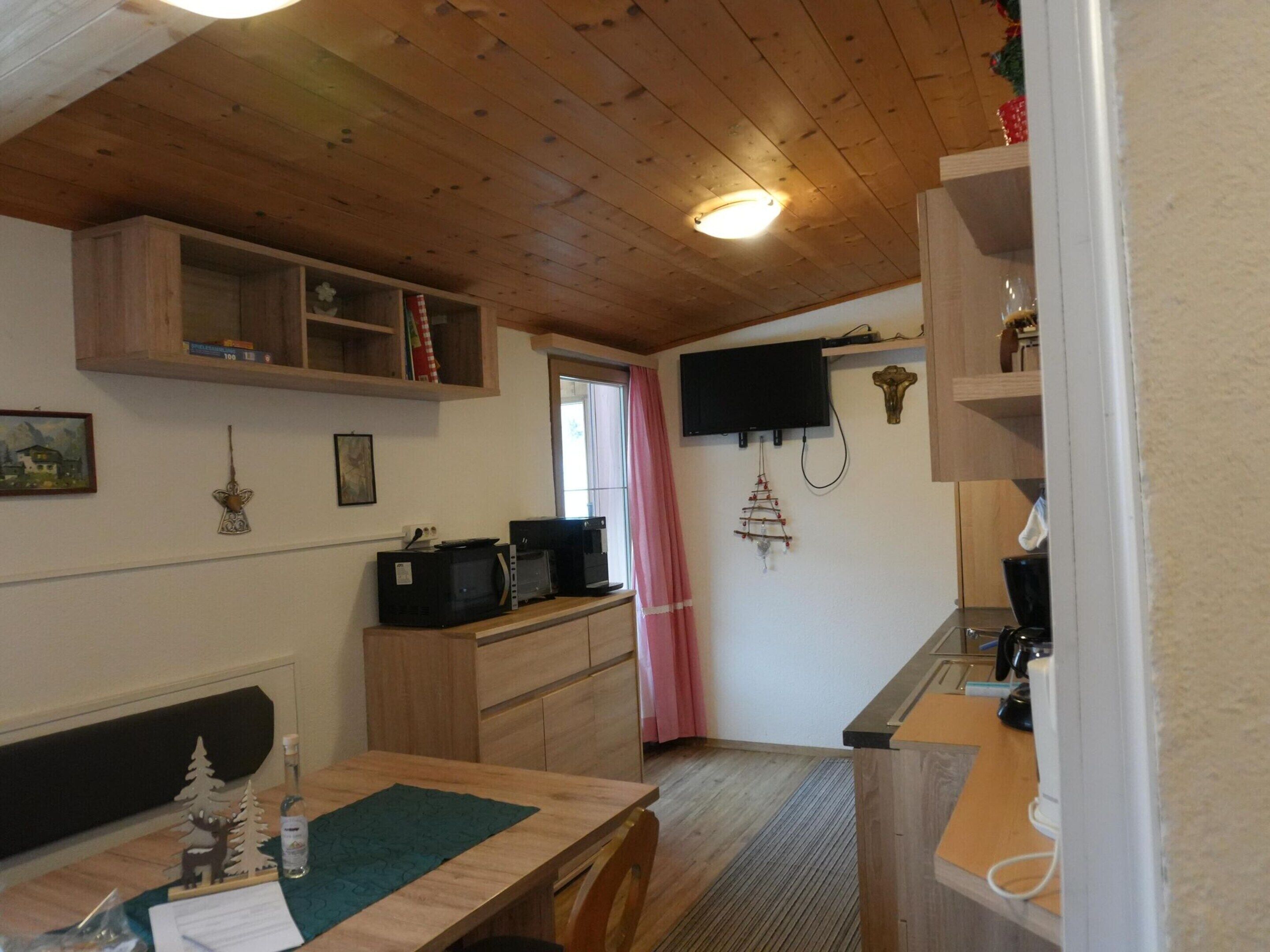 A compact kitchen with wooden cabinets, a microwave, a coffee maker, and a television mounted on the wall.