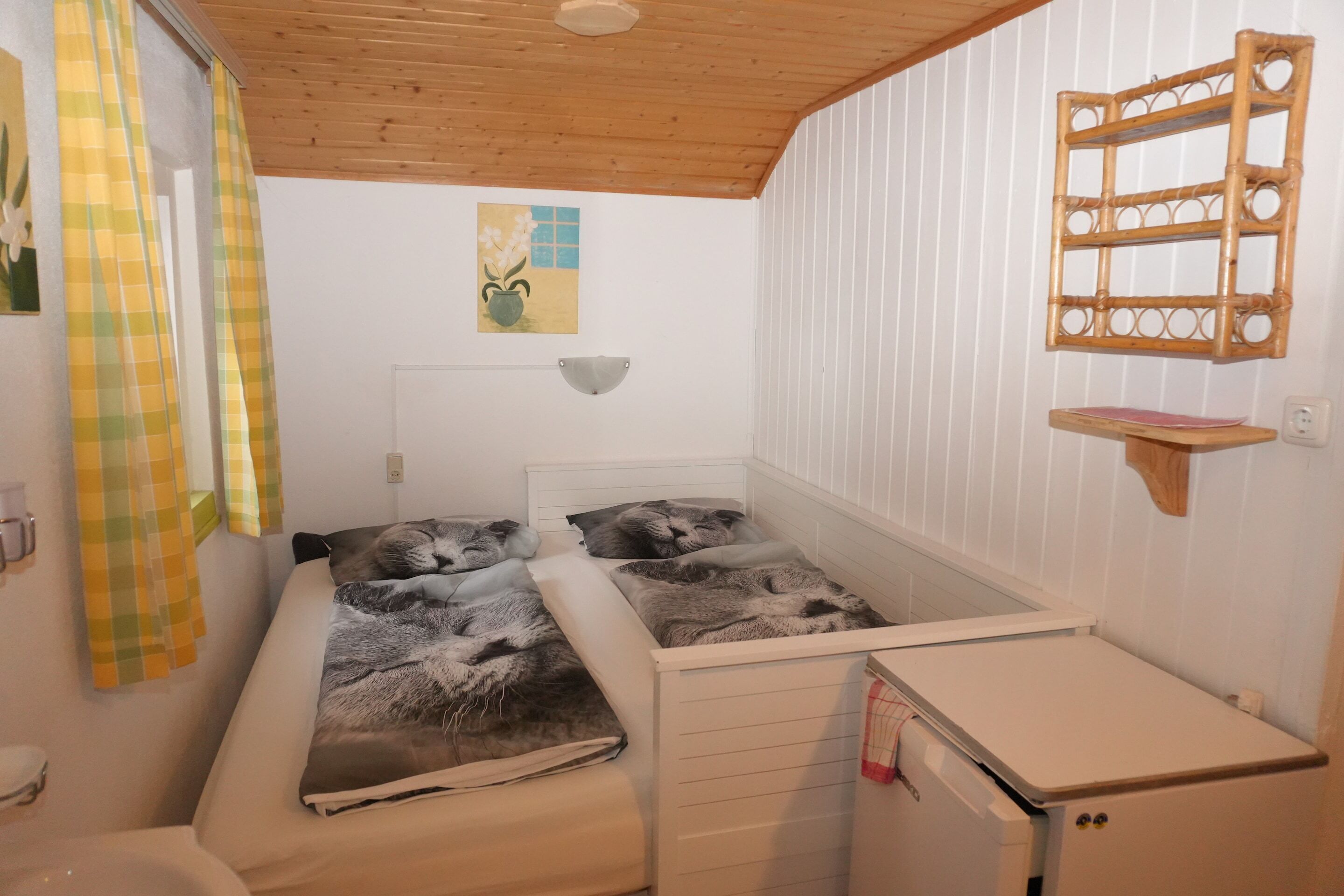 Une petite pièce agréable et chaleureuse, avec un lit, une petite table, une étagère fixée au mur et une fenêtre avec des rideaux.
