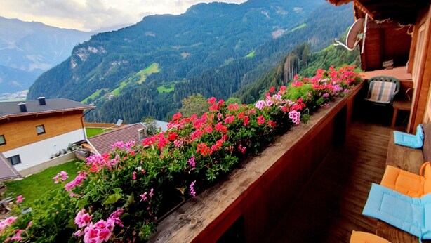 Un balcon doté d’une balustrade en bois, offrant une vue sur un paysage montagneux parsemé de maisons et de verdure.