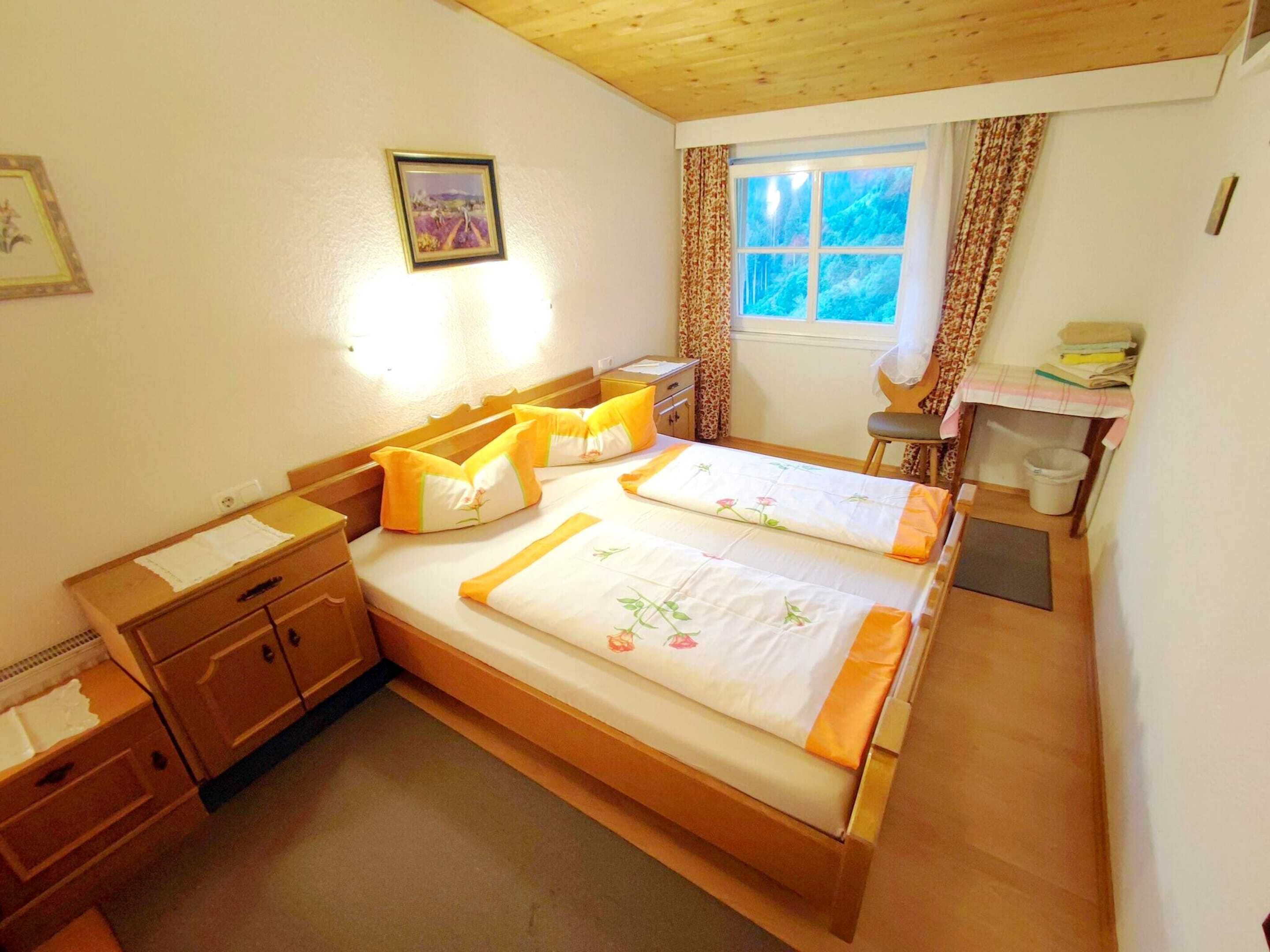Een slaapkamer met twee bedden, houten meubels, een raam met gordijnen en een klein bureau met stoel.