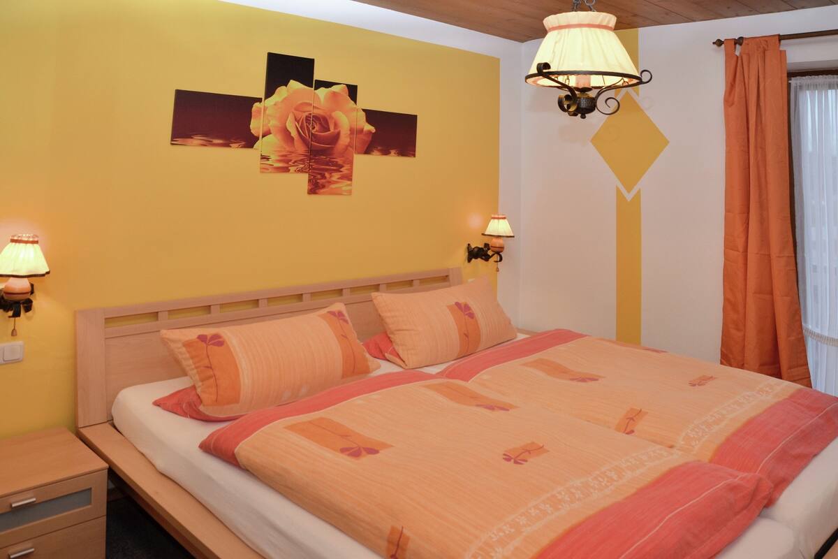A bedroom with a bed, two bedside lamps, a nightstand, and a wall with a floral artwork.
