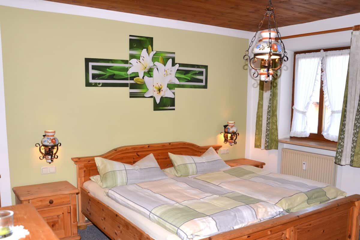 A bedroom with a wooden bed, two bedside tables, a wall-mounted lamp, and a window with curtains.