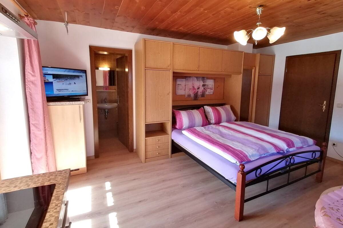 A bedroom with a bed, wooden wardrobe, a television, and a bathroom.