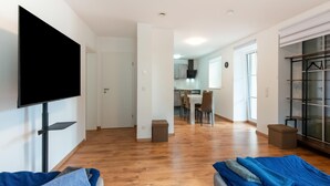 A modern apartment with a flat-screen TV mounted on the wall, a dining area with a table and chairs, and a large wardrobe with a mirror. - Lovely Holiday Home in Haunsheim (Haunsheim)