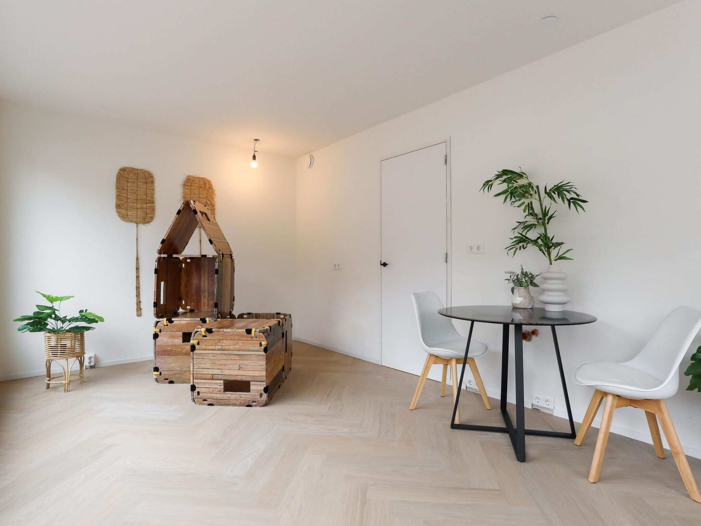 A modern living room with a wooden playhouse, a round table with chairs, and potted plants.