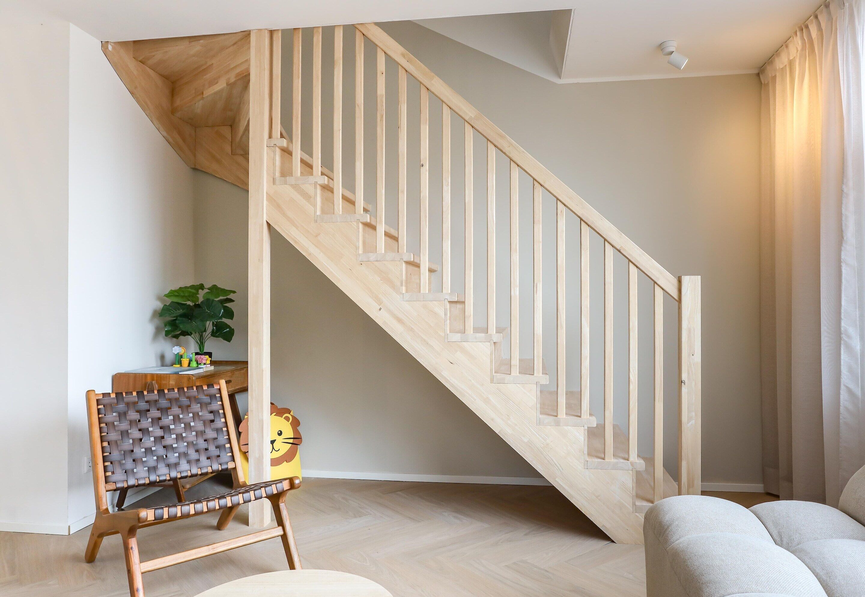 A wooden staircase in a room with a herringbone-patterned chair, a small table with decorative items, and a sofa.