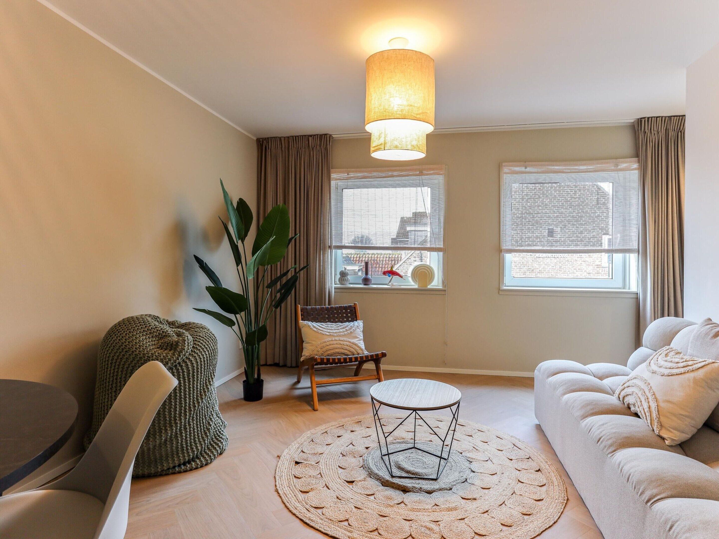 A modern living room with a round coffee table, a sofa, a chair, and a large plant.
