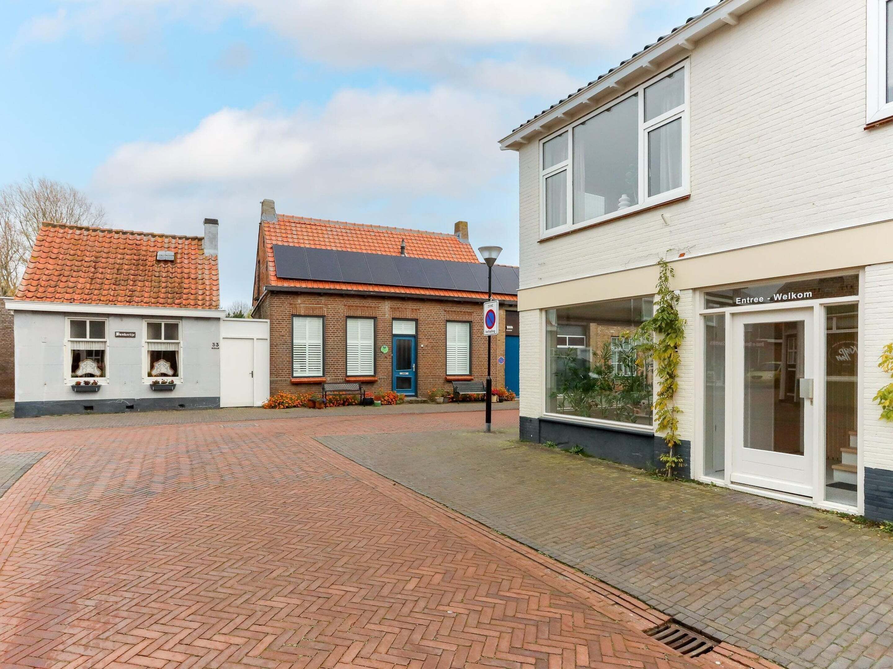 Straßenansicht mit einem Gebäude, das eine blaue Tür und ein Schild mit der Aufschrift 'Entree Welkom' hat.