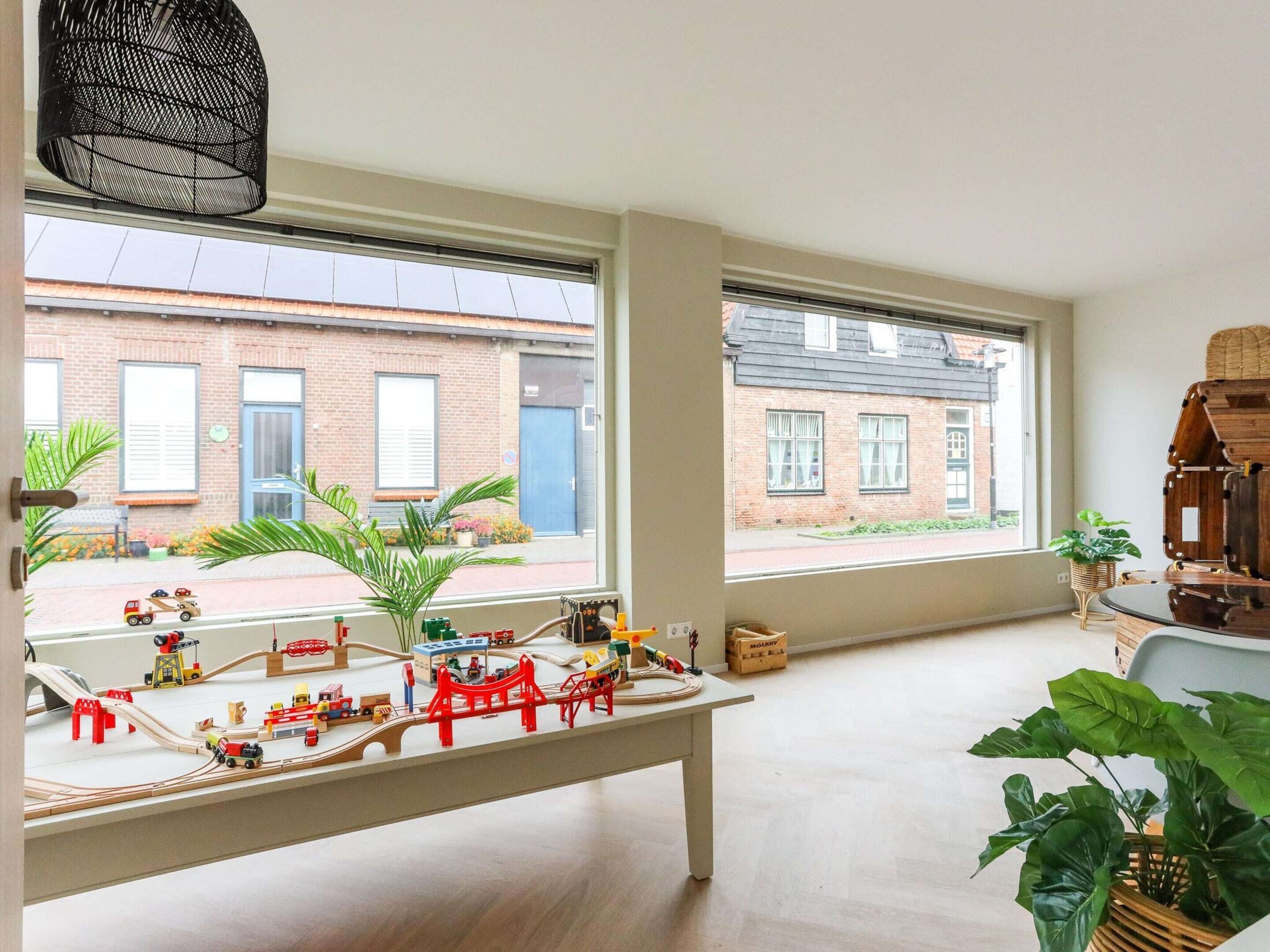 Una habitación espaciosa con ventanas amplias, un tren modelo sobre una mesa y una planta en maceta.