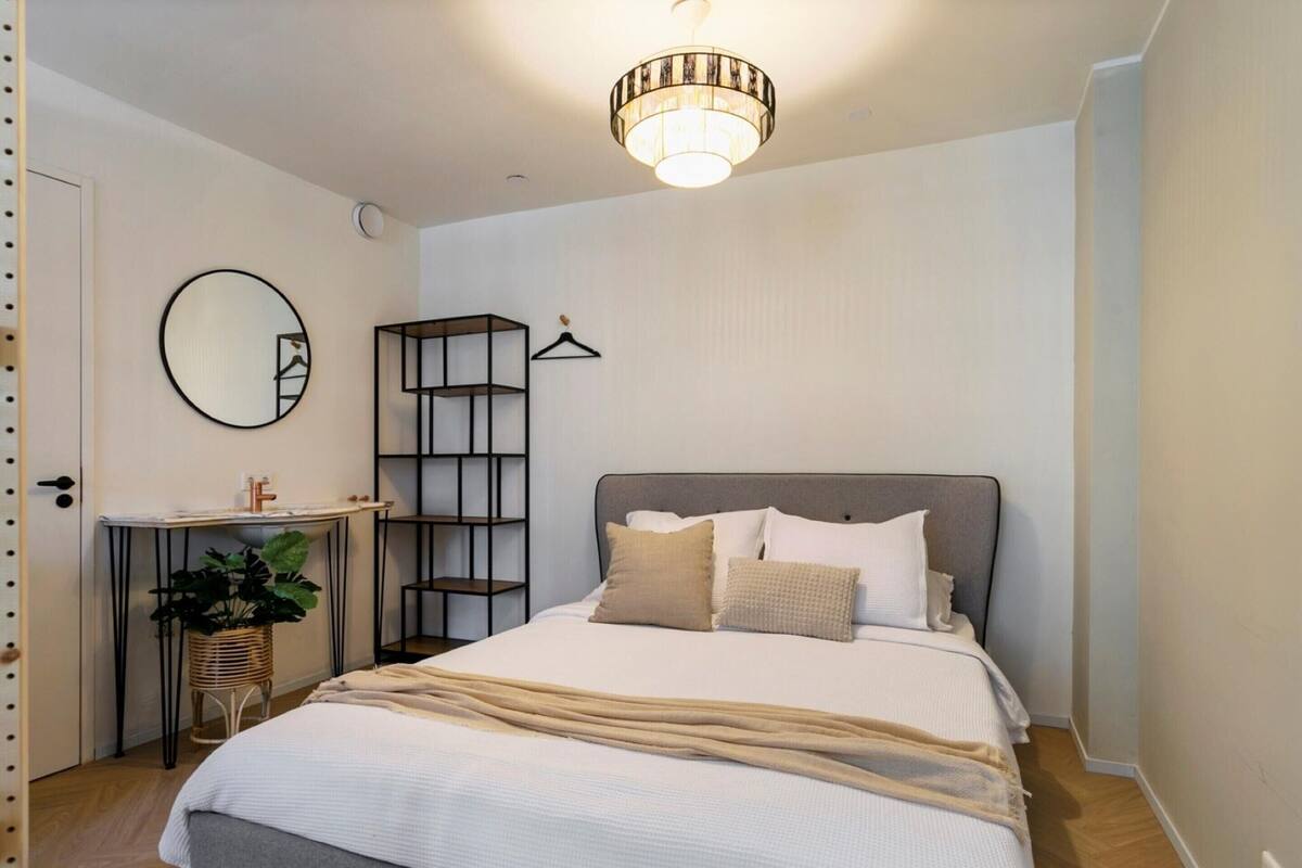 A bedroom with a bed, bedside table, mirror, and a hanging light fixture.