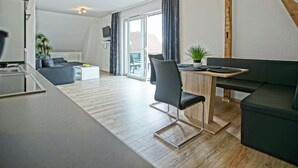 A modern living room with a sofa, a dining table, and a kitchen area. - Unterkunft in Monkebude mit Eigenem Garten (Monkebude)