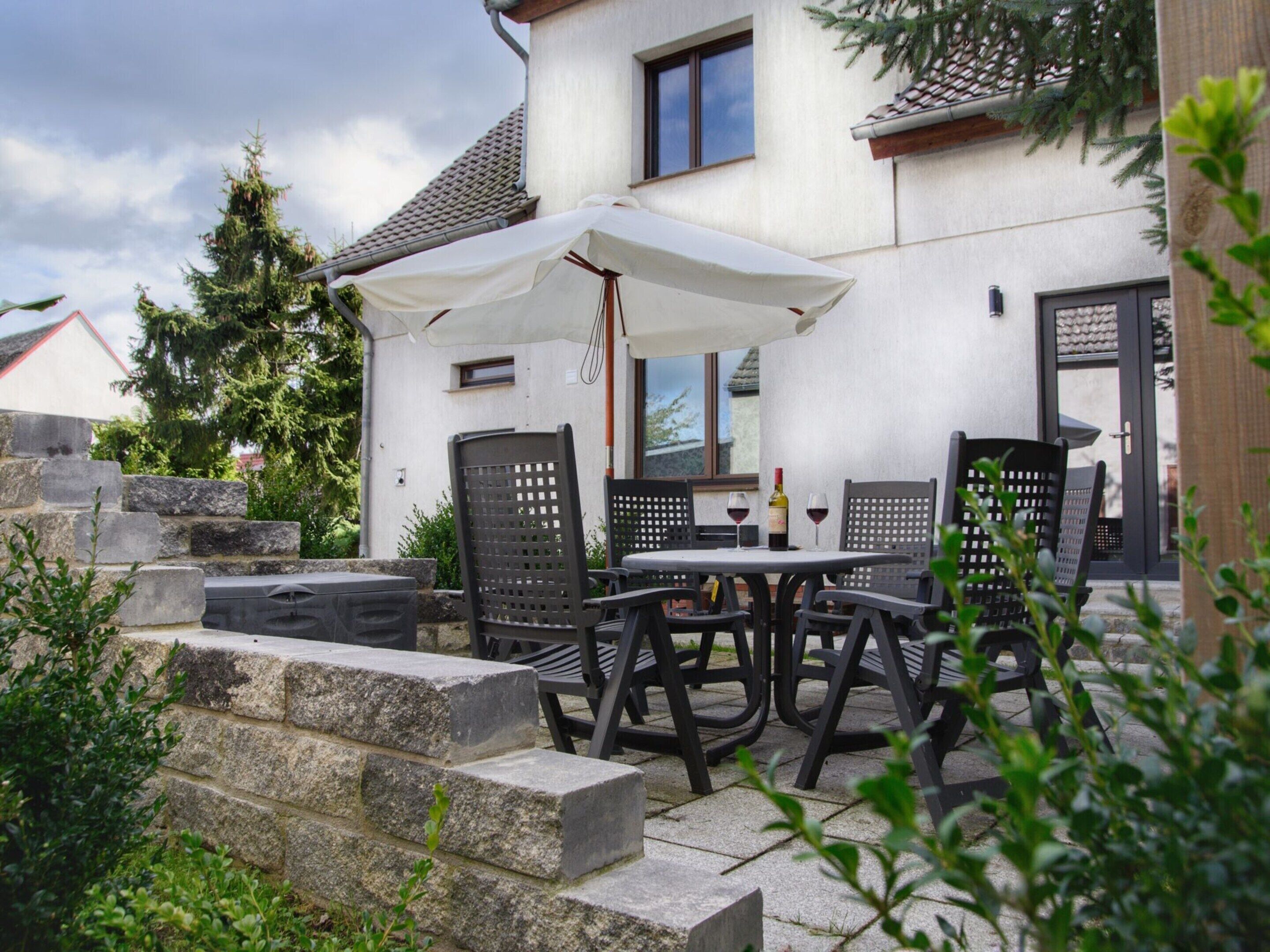 An outdoor patio with a table and chairs, a white umbrella, and a stone wall.
