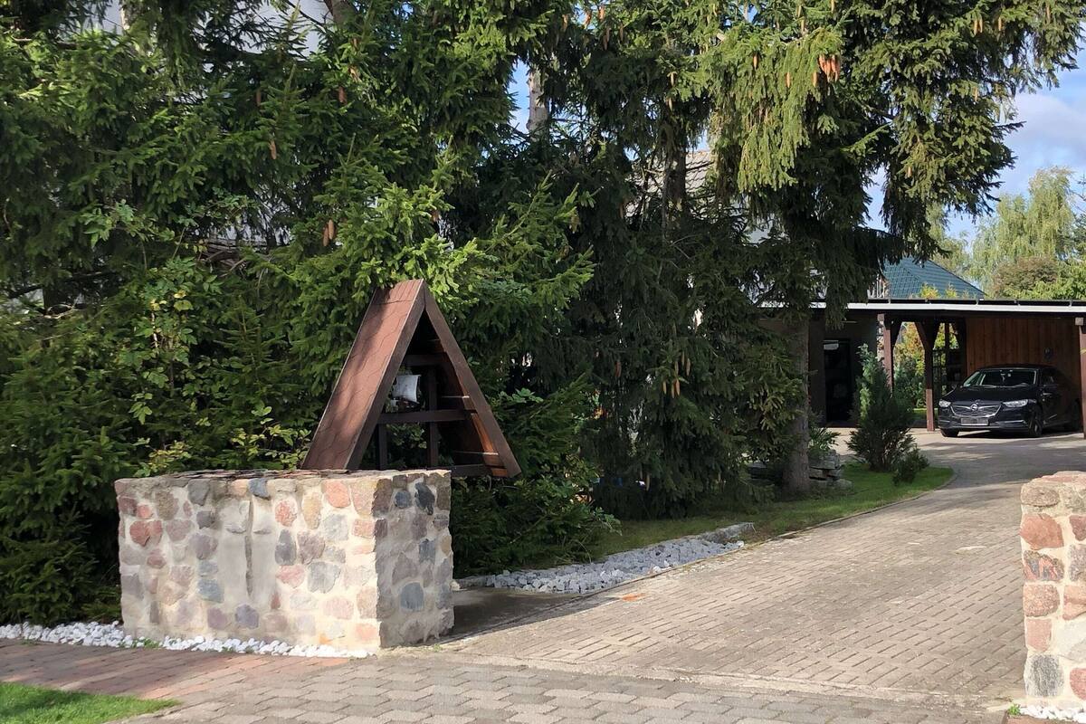 A stone structure with a triangular roof, a paved driveway, and a building with a covered entrance.