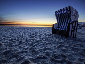 Ein Liegestuhl mit gestreifter Auflage direkt am Sandstrand.