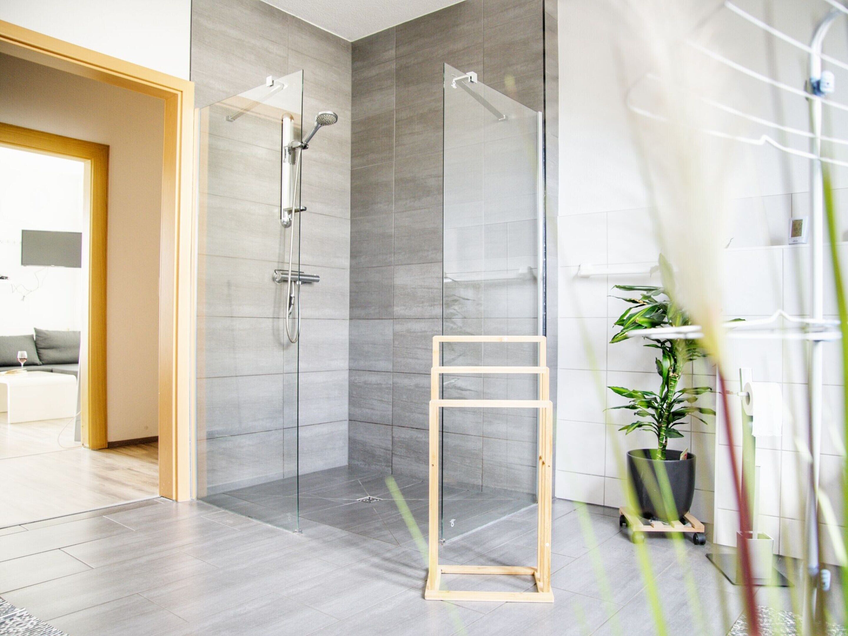 A modern bathroom with a glass shower enclosure, a wooden ladder, and a potted plant.