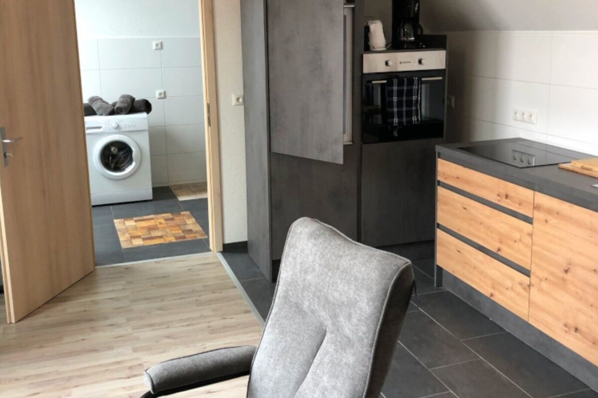 A modern kitchen with a built-in oven, a coffee machine, and a wooden cabinet.