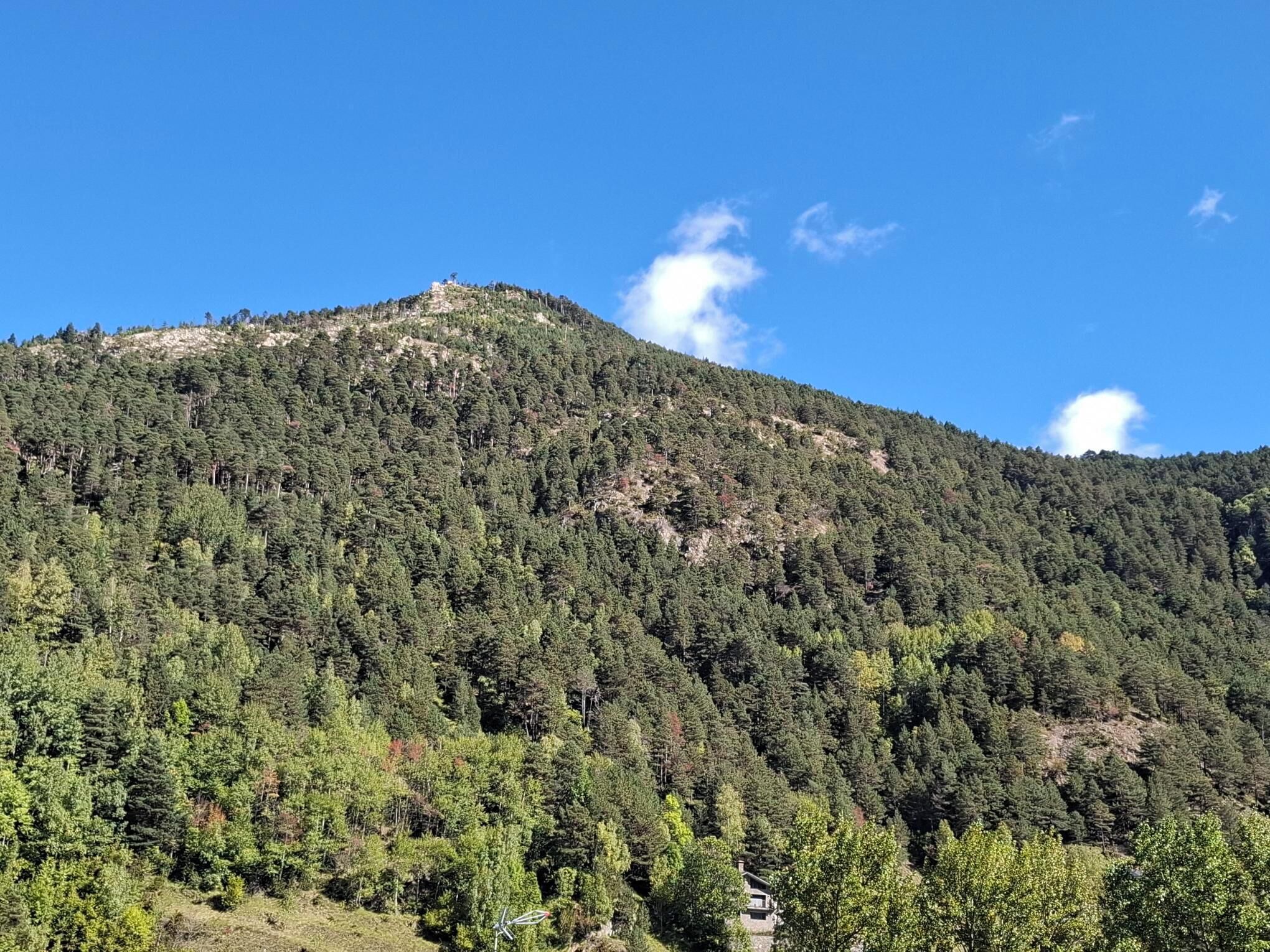 Una montaña cubierta de denso bosque con un pequeño edificio en su base.