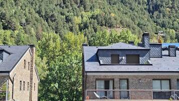 A building with a stone facade and a balcony, set against a backdrop of a forested mountain.