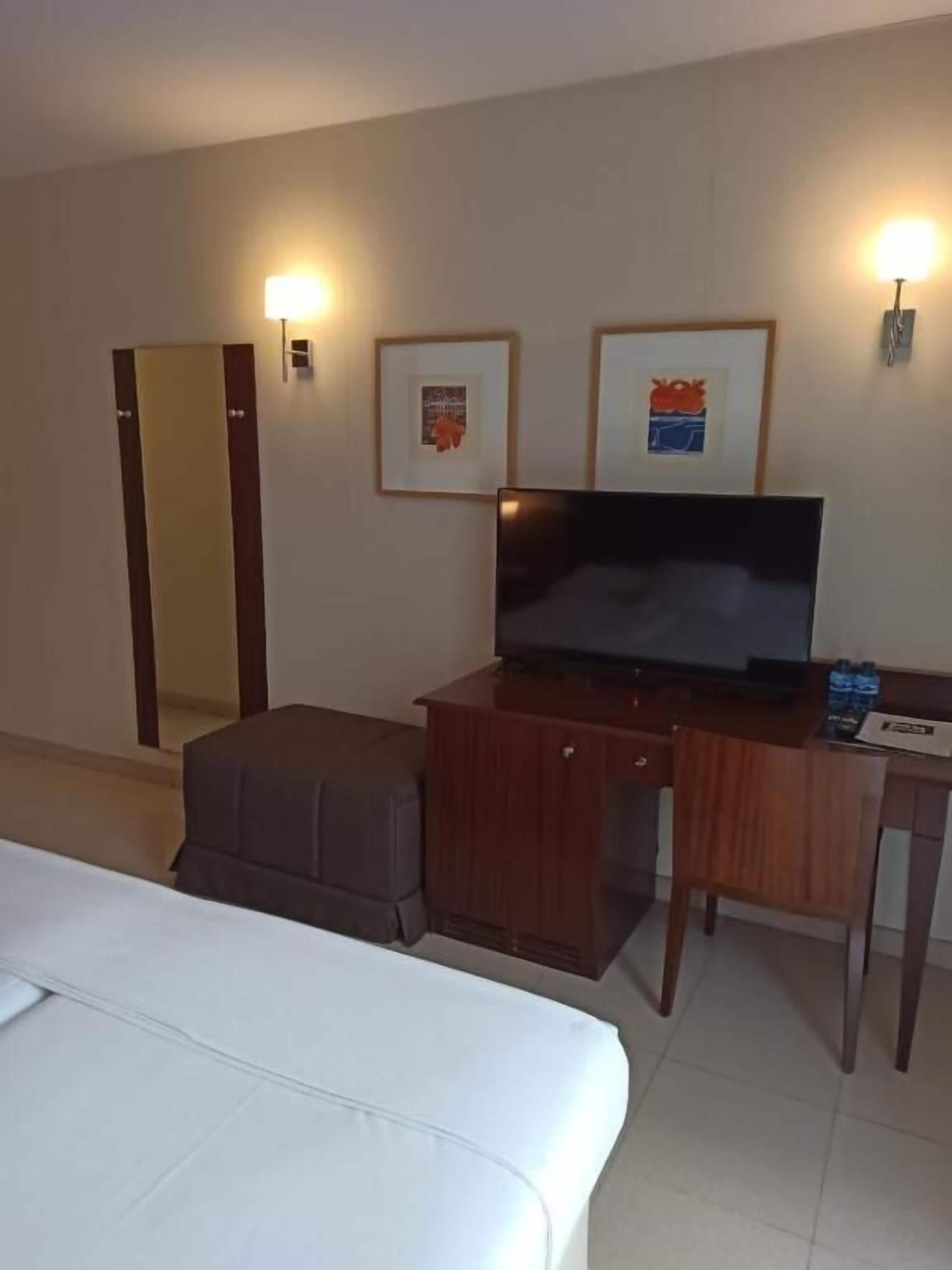 Una camera d'albergo con un letto, una scrivania con televisore e quadri appesi al muro.