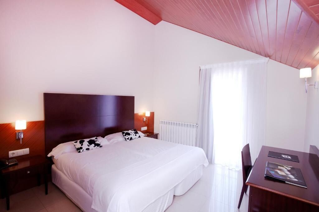 A hotel room with a large bed, a wooden headboard, a desk with a chair, and a window with curtains.