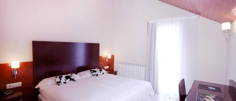 A hotel room with a large bed, a wooden headboard, a desk with a chair, and a window with curtains.