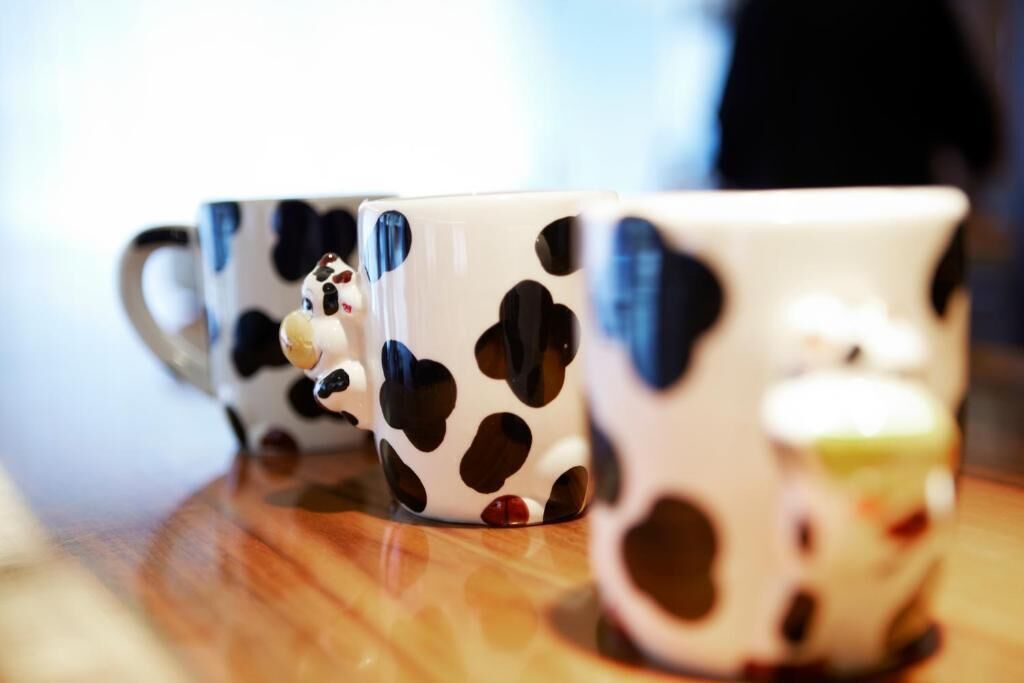 Three white mugs with black spots and a cow design on a wooden surface.