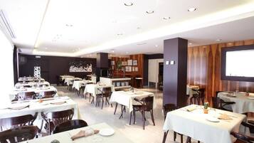 Un comedor amplio con varias mesas y sillas, una pantalla grande en la pared y una pared de acento de madera.