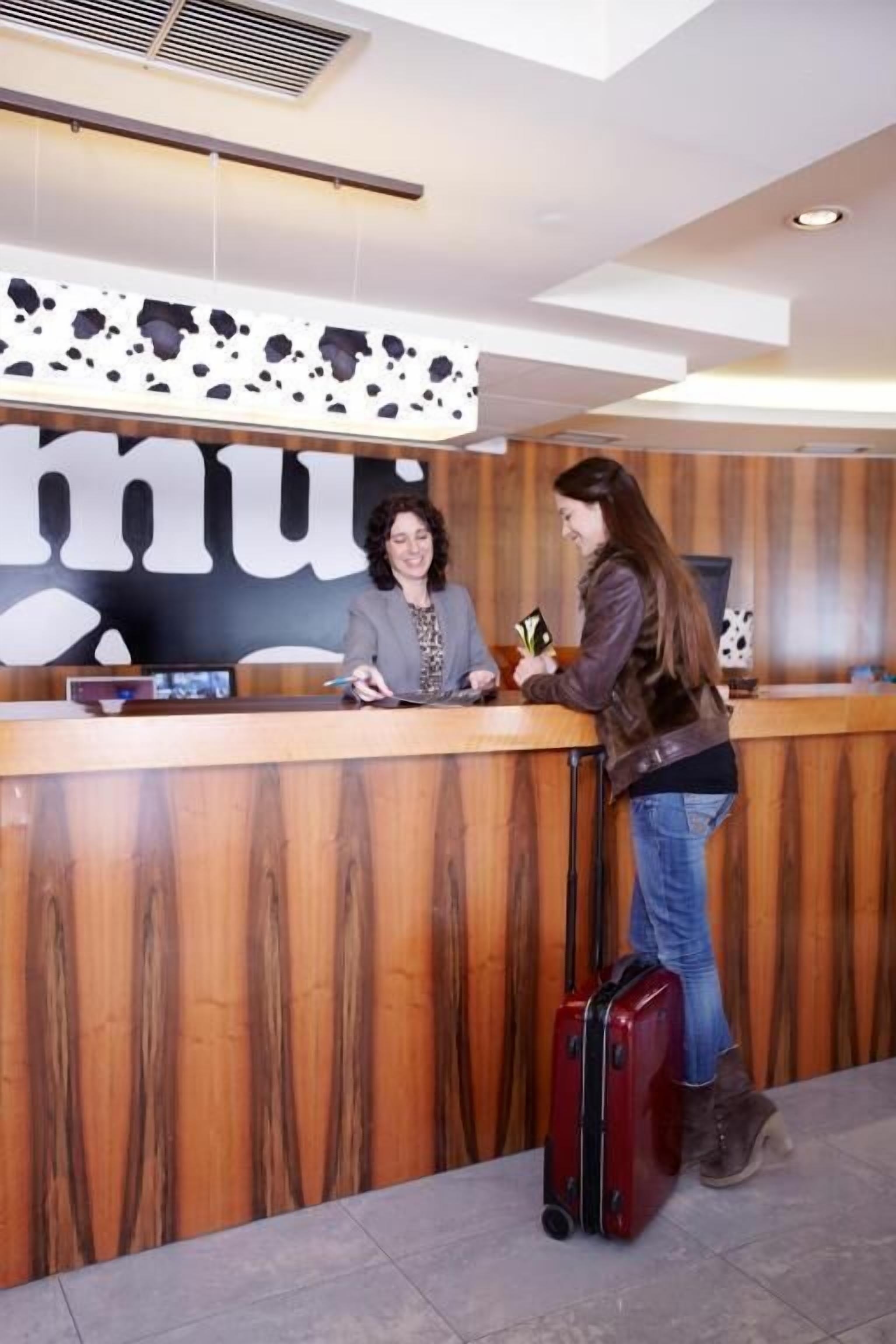 Een receptiebalie met een houten afwerking, een digitaal scherm en een bordje met het woord 'nu'.