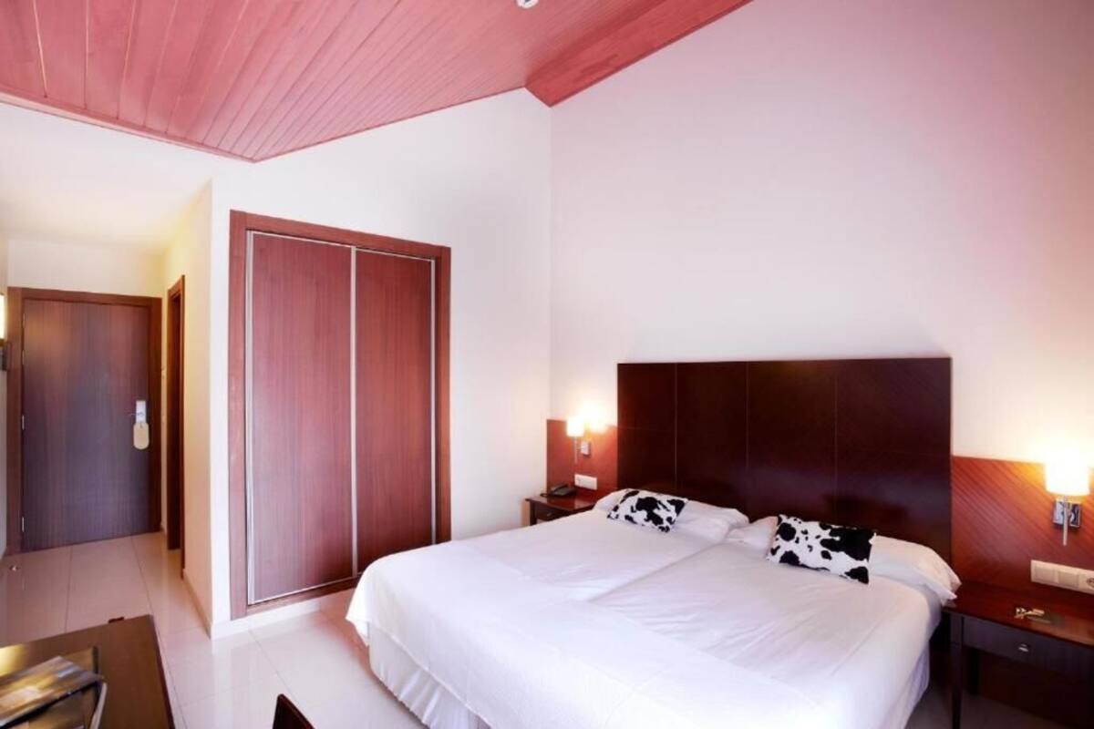 A hotel room with a large bed, wooden headboard, bedside lamps, and a wardrobe.