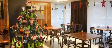 Een restaurantgedeelte in een hotel, versierd met een kerstboom, versieringen en een kerstman. Tafels en stoelen staan klaar voor de gasten.