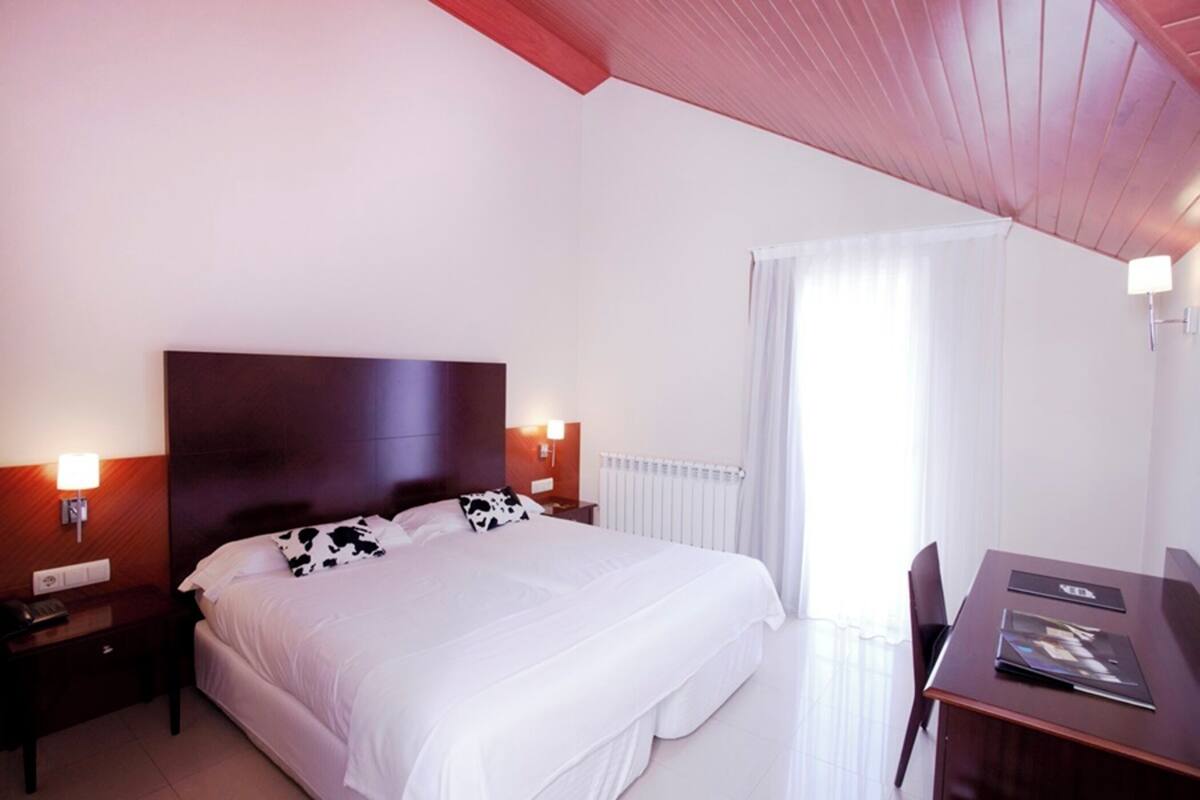 A hotel room with a large bed, bedside tables, a desk, and a window with curtains.