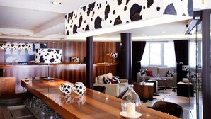 A modern hotel lobby with a wooden reception desk, cow-print decor, and a seating area with sofas and a glass partition. - Hotel Mu (La Cortinada)