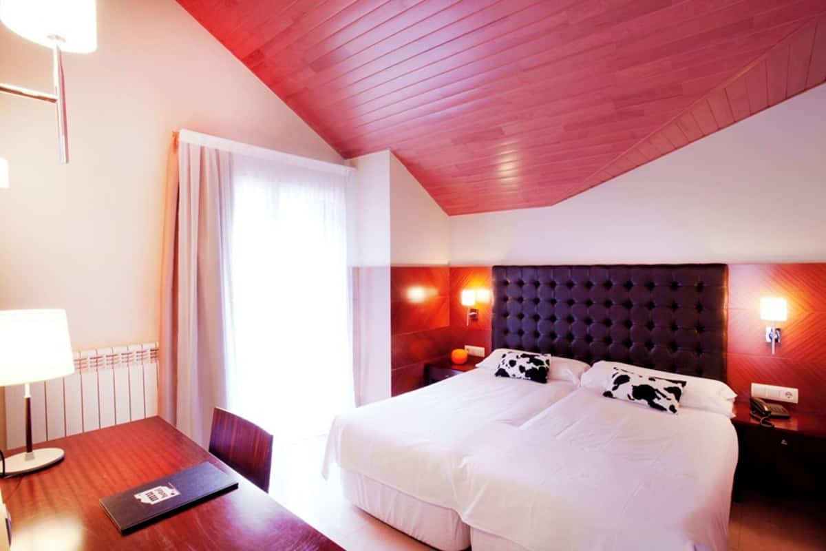 A hotel room with a large bed, a wooden desk, a lamp, and a window with curtains.