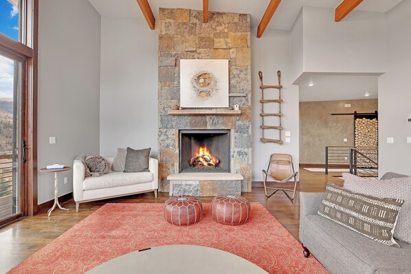 A living room with a stone fireplace, a white sofa, a grey sofa, and a red rug. - Luxurious Contemporary Home (Silverthorne)