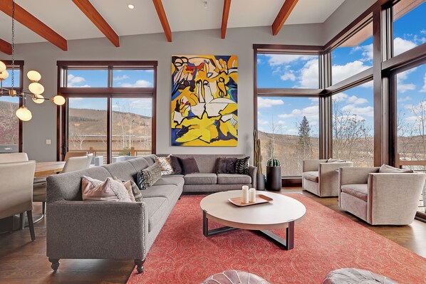 A spacious living room with a gray sofa, a round coffee table, and a large abstract painting on the wall.