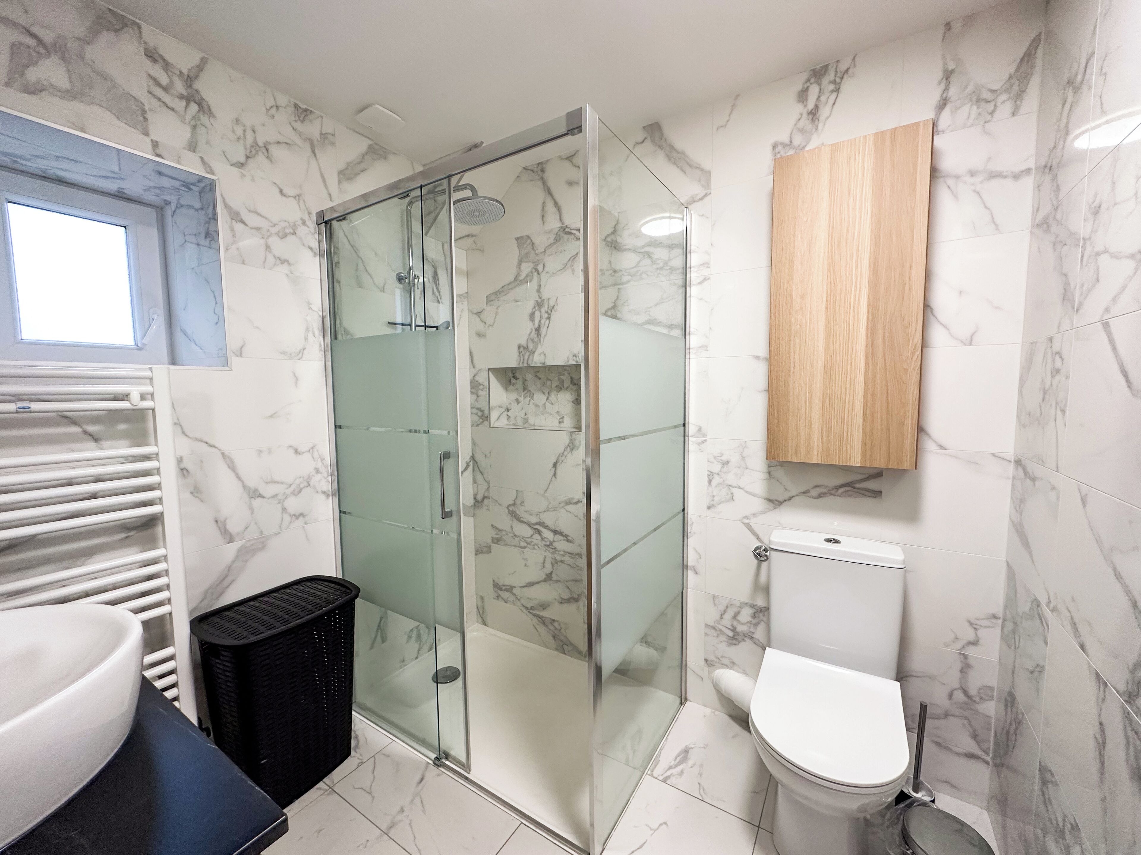 A bathroom with a glass-enclosed shower, a white toilet, and a wooden cabinet above the toilet.