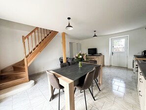A modern kitchen with a dining area, wooden staircase, and a TV on a wooden cabinet. - L'Évasion Gelinoise (La Tour-Saint-Gelin)
