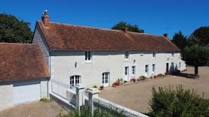 A white stone building with a red-tiled roof, a white garage door, and a gravel driveway. - L'Évasion Gelinoise (La Tour-Saint-Gelin)