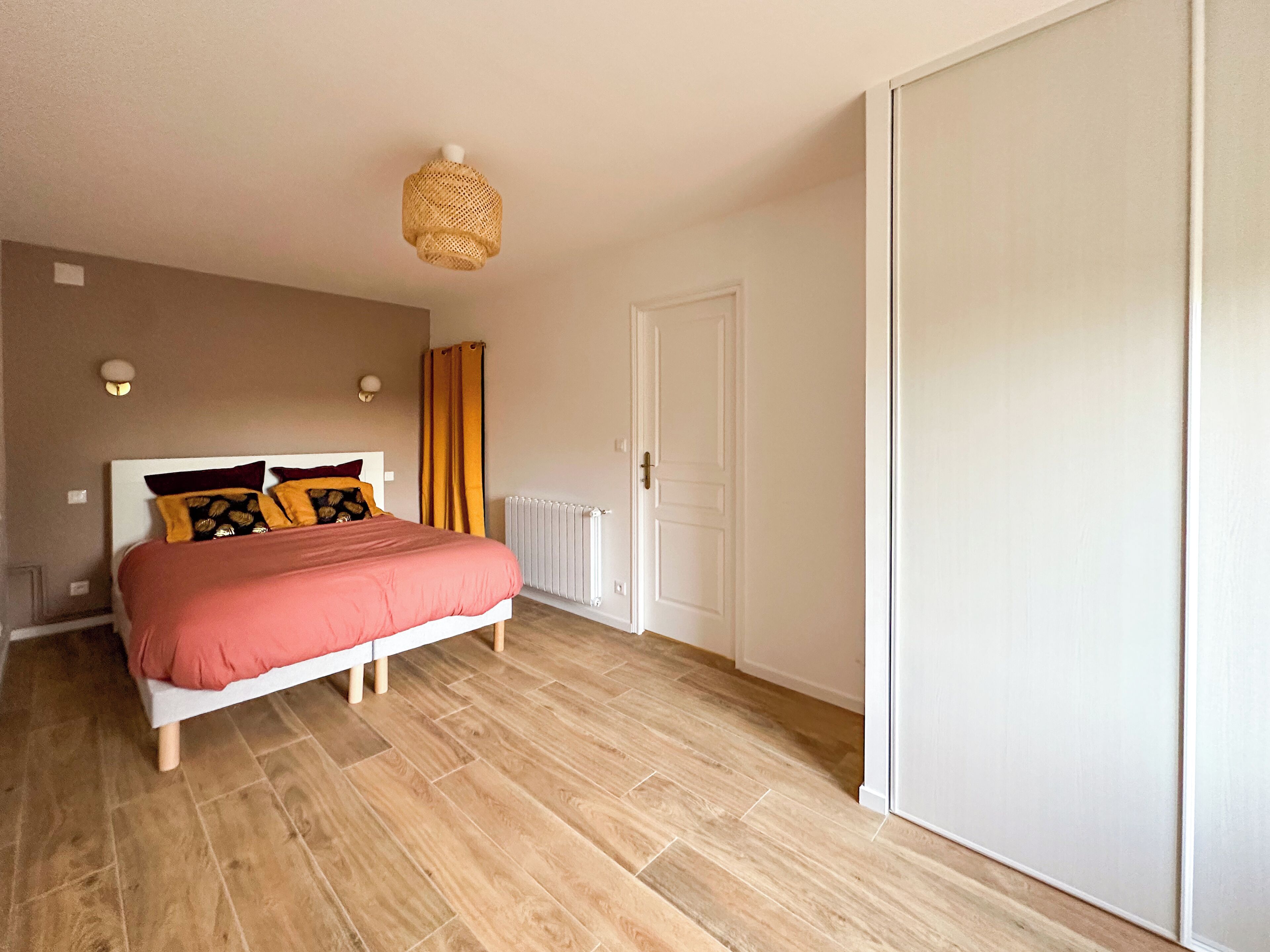 A bedroom with a bed, wooden floor, a white door, and a ceiling light fixture.