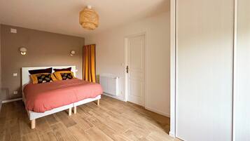 A bedroom with a bed, wooden floor, a white door, and a ceiling light fixture.