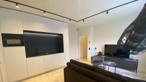 A modern living space with a kitchen, a large flat-screen TV, a sofa, and a fan. - Modern Holiday Home in Bazel With Garden (Kruibeke)