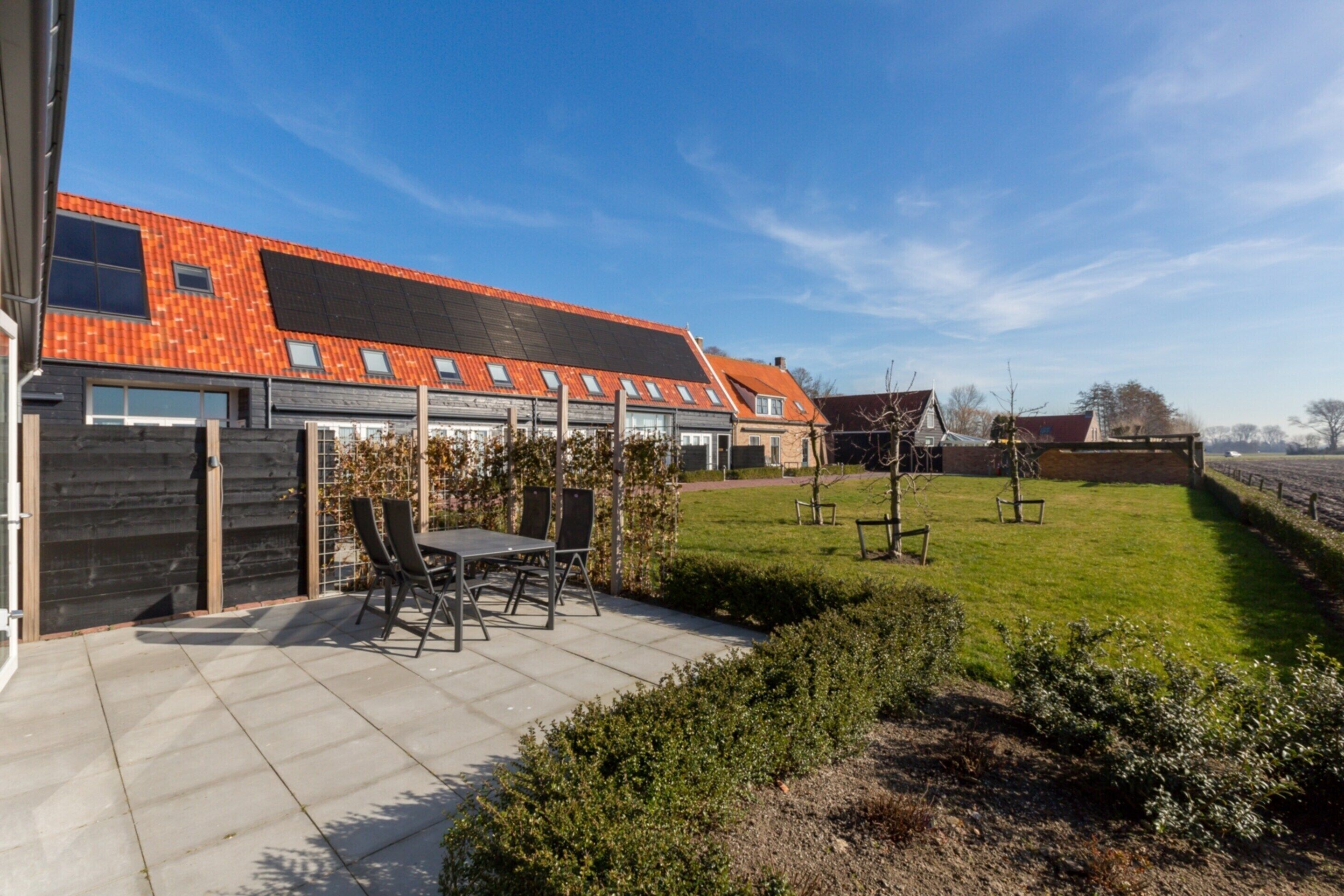 A modern building with a red-tiled roof, a patio area with a table and chairs, and a well-maintained lawn.
