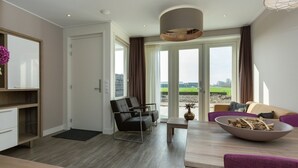 A modern living room with a sofa, a dining table, and a kitchen area. - Luxury Apartment With sun Shower at the Edge of the Beautiful Oostkapelle (Oostkapelle)