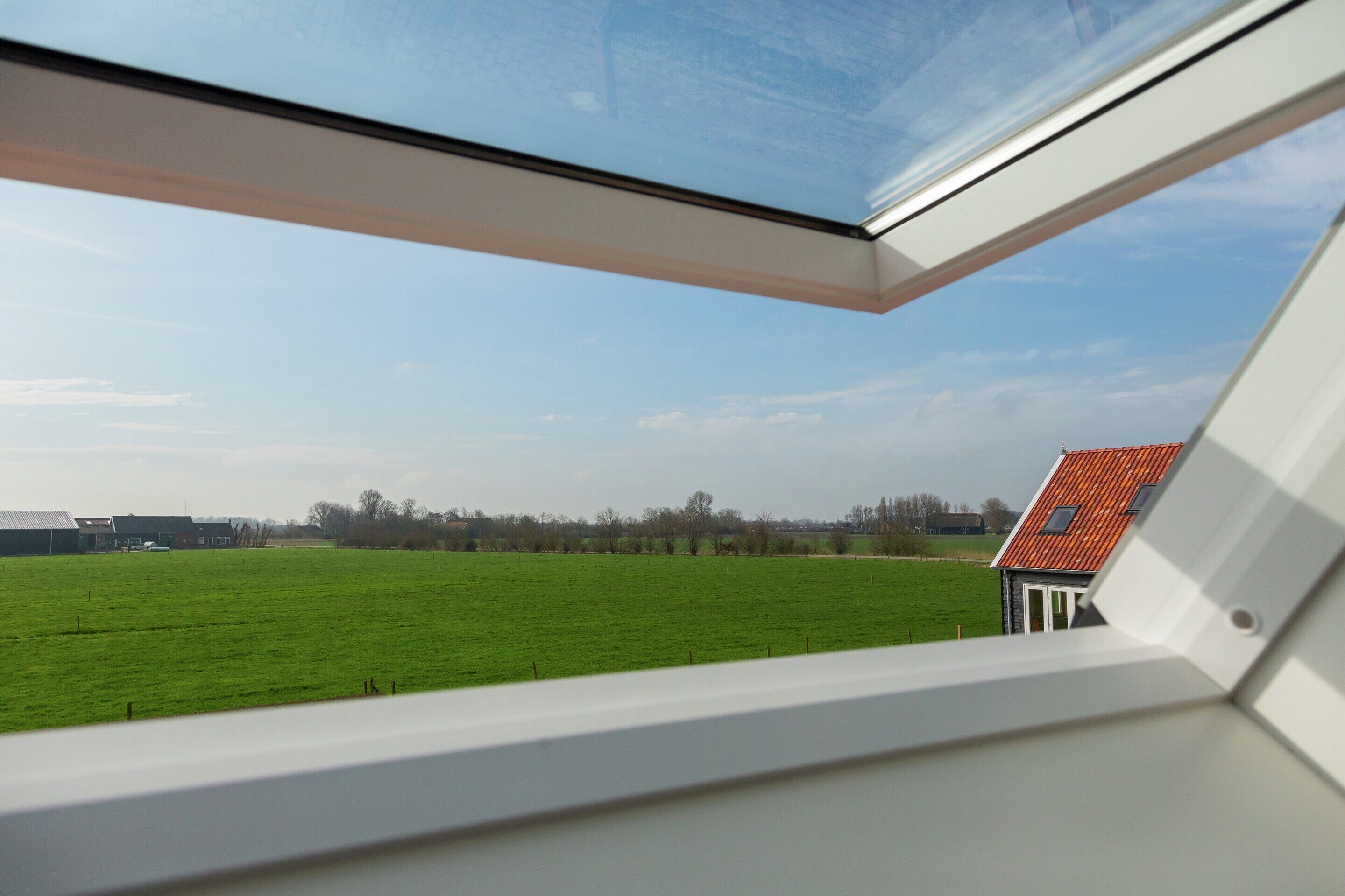 Blick aus einem Fenster auf einen wolkenlosen Himmel, ein grünes Feld und ein Gebäude mit rotem Dach.