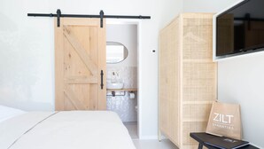 A modern bedroom with a bed, a wooden sliding door leading to a bathroom, a television mounted on the wall, and a wicker storage unit. - Pleasaing Holiday Home in Oostkapelle Near Centre (Oostkapelle)