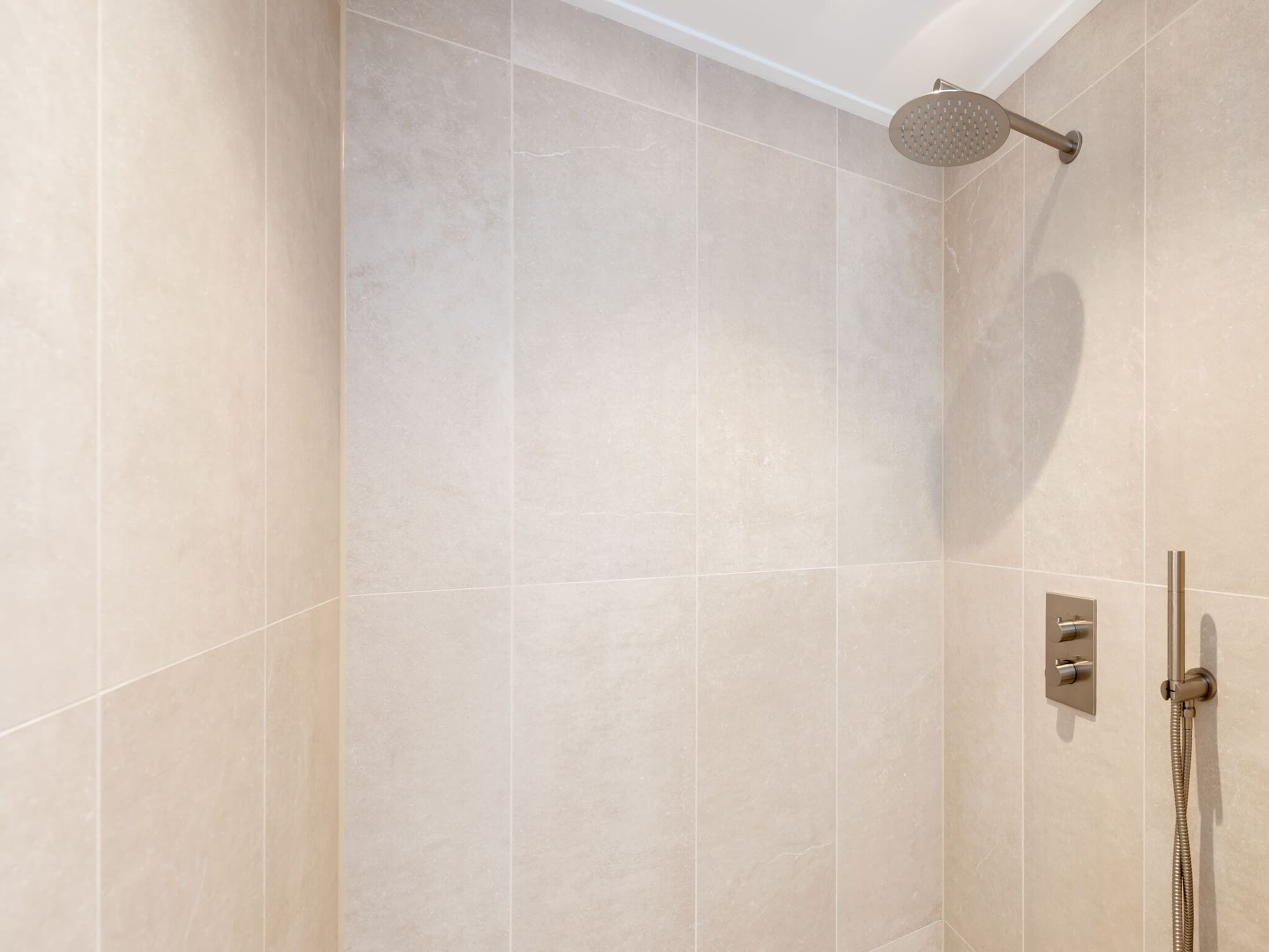 A modern bathroom with beige tiles, a handheld showerhead, and a wall-mounted control panel.