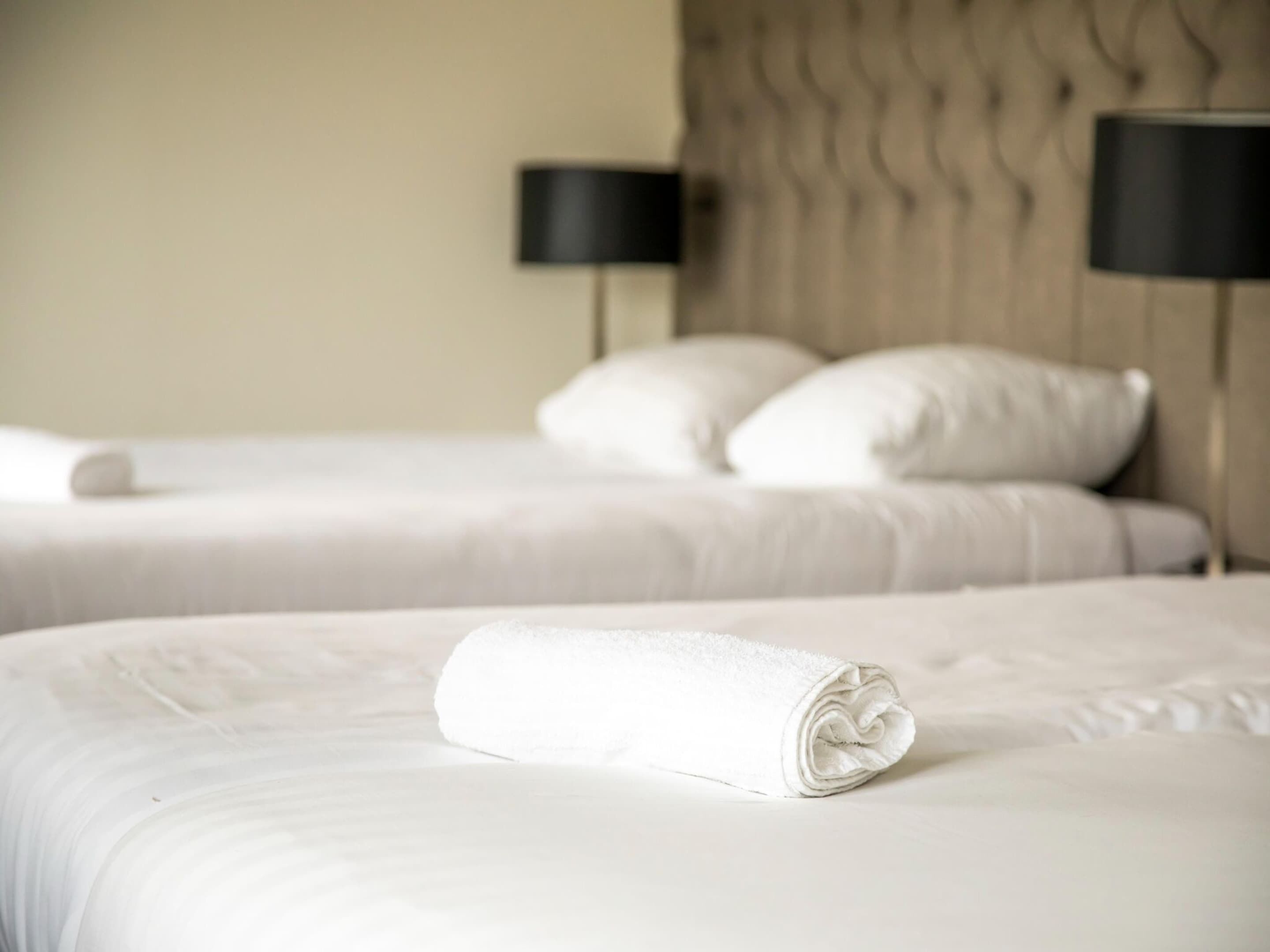 A hotel room with two beds, each with a neatly folded white towel.